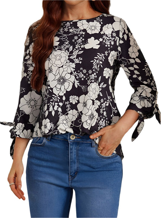 Woman wearing a black and white floral blouse with tied sleeves and relaxed fit.
