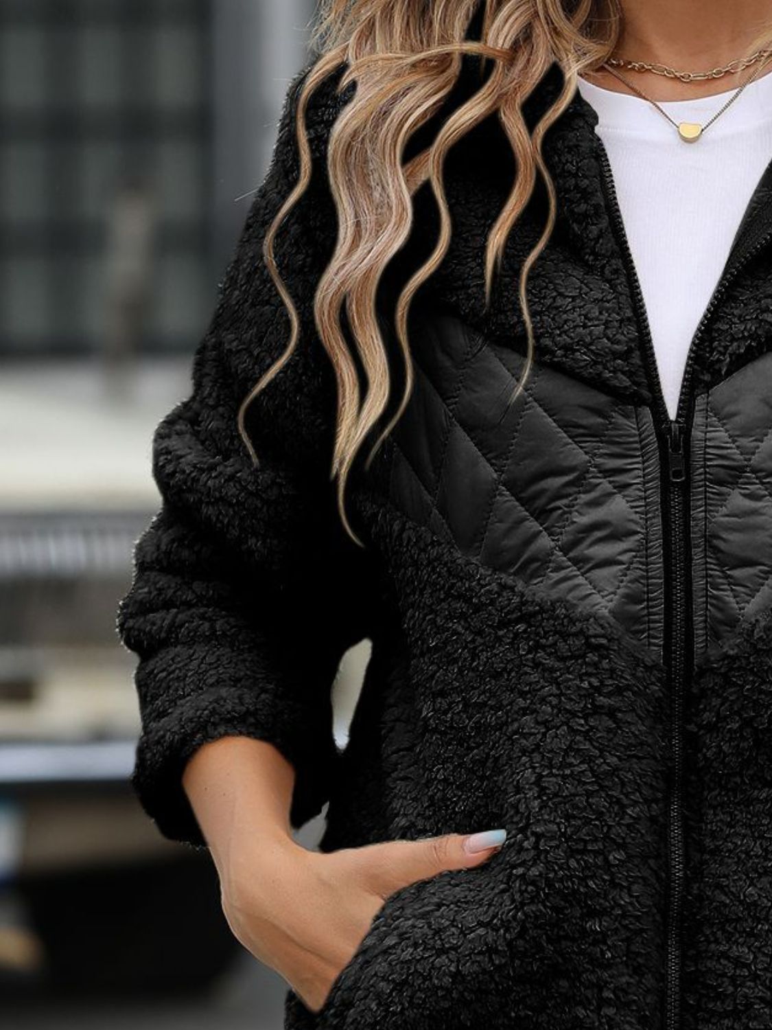 Women’s zip-up fuzzy jacket in black with hood and pockets for warmth.