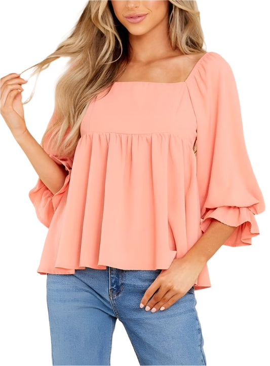 Woman wearing a coral ruffled babydoll blouse with square neck and flowy fit.