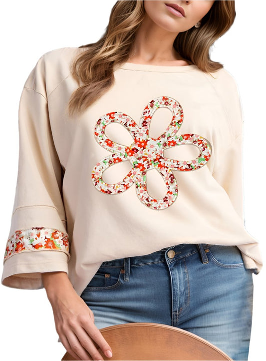Woman wearing an ivory floral applique blouse with exposed seams and a relaxed fit.