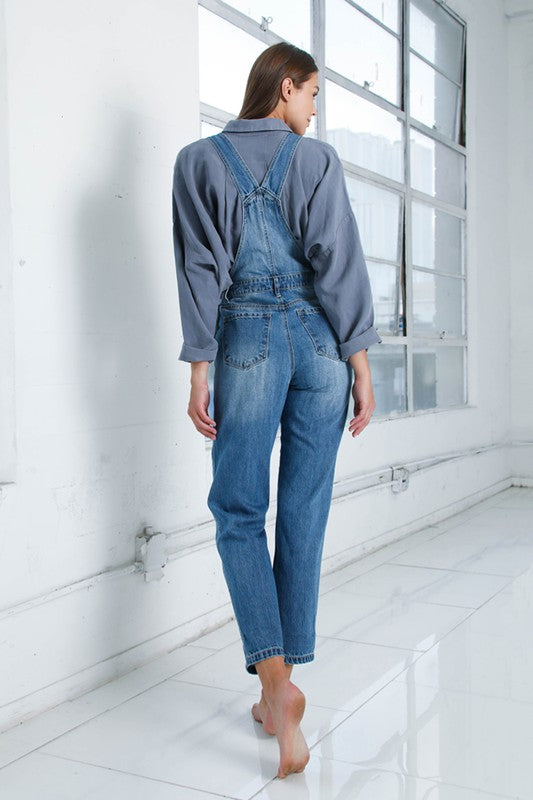 Adjustable shoulder straps on medium wash women’s denim jumpsuit.