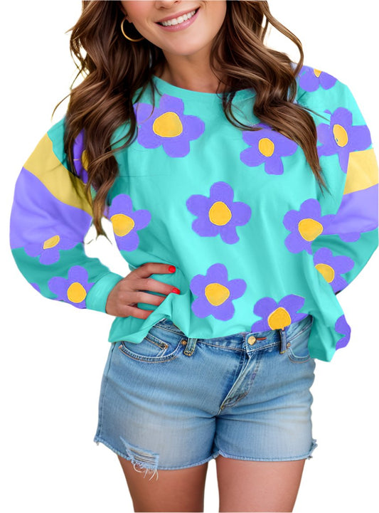 Woman wearing a playful floral long sleeve top with bold purple and yellow flowers on a teal background.