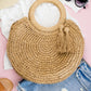 Woven straw tote bag with round handles and tassel accents.