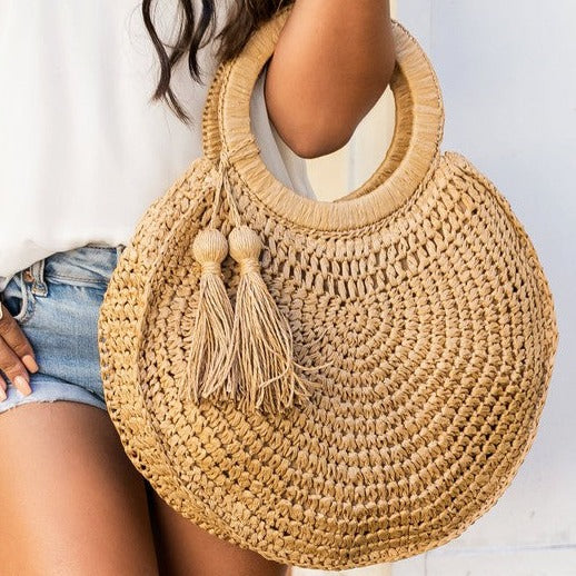 Woven straw tote bag with round handles and tassel accents.