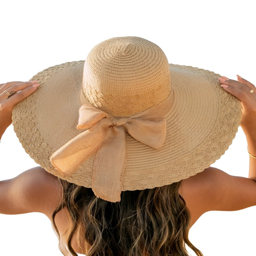 Woman wearing a wide brim straw hat with a large bow, facing the beach.