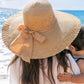 Lady on the beach sporting a wide brim straw hat with a beautiful bow.