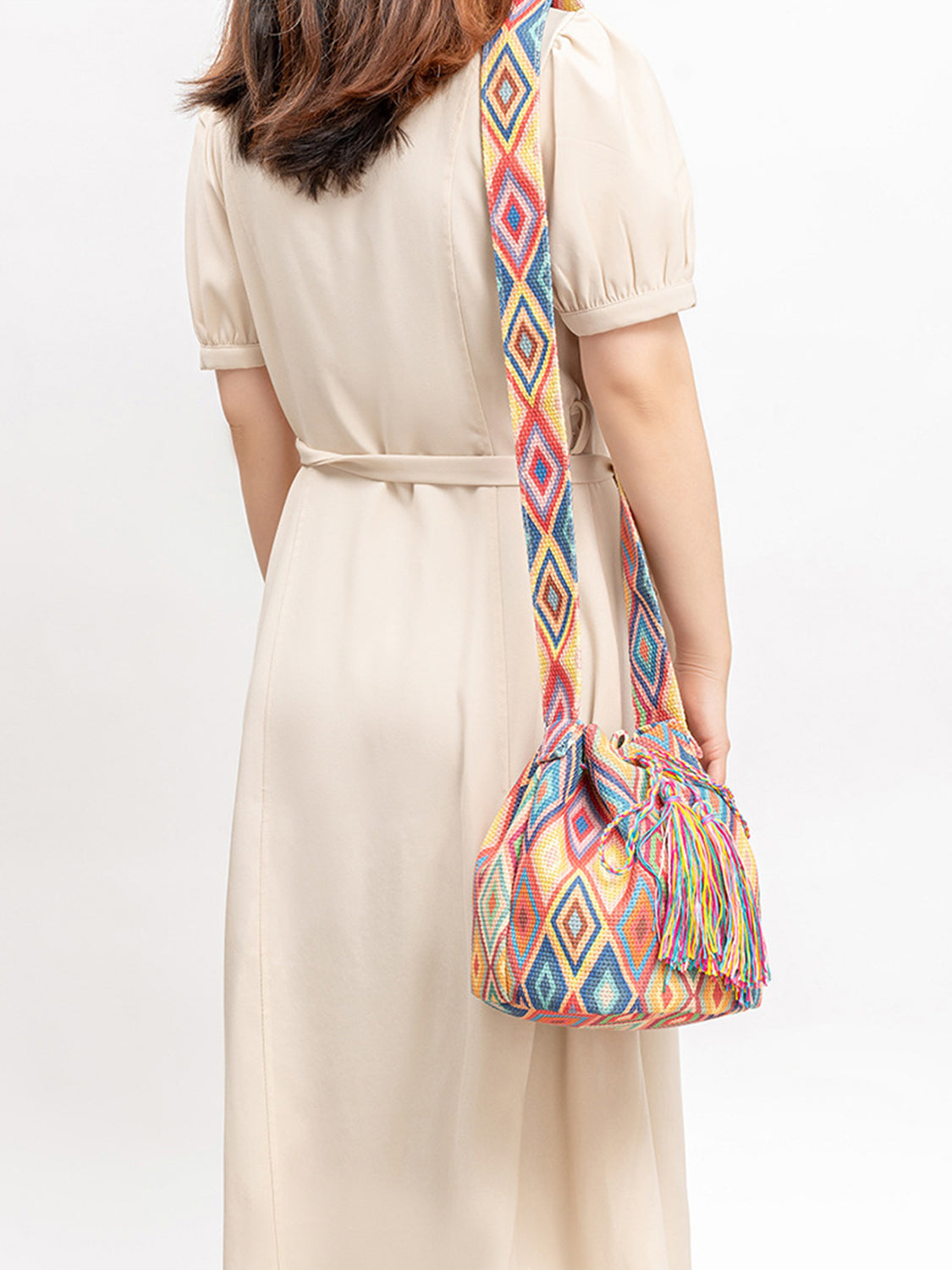 Multi-colored geometric patterned bucket bag with tassels.