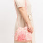 Cream and pink bucket bag with woven fabric and tassel accents.