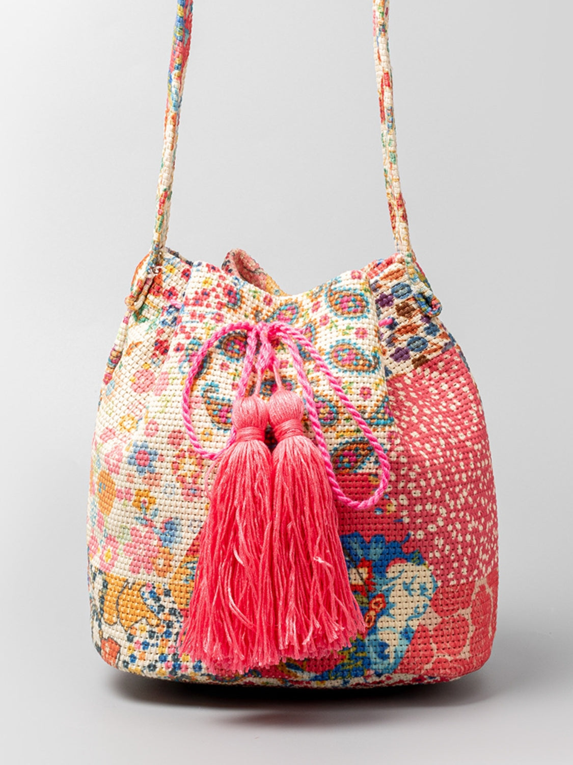 Pink and cream patterned bucket bag with drawstring closure and tassels.