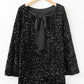 Festive black sequin dress with a bow-back and bell sleeves.