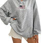 Woman wearing a gray hoodie with an embroidered American flag on the chest.
