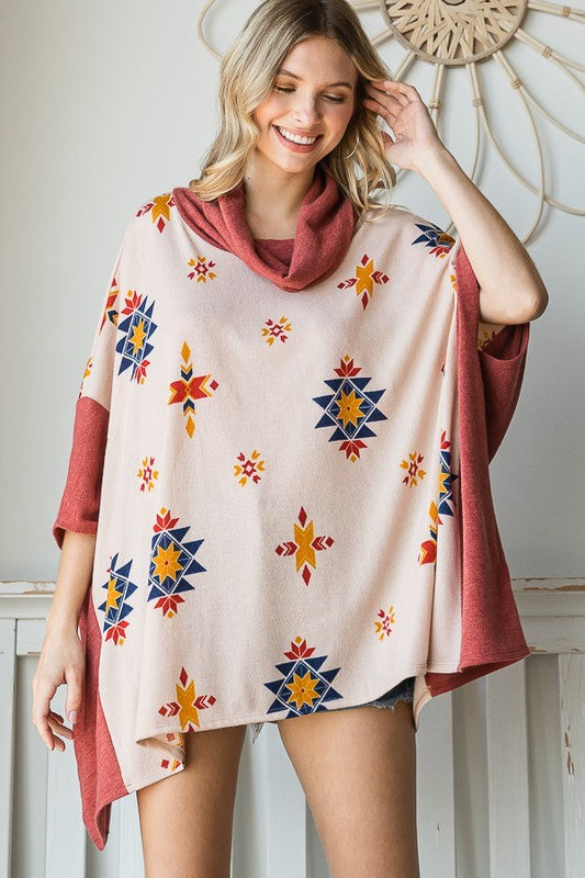 Woman wearing a beige Aztec print cowl neck poncho with rust accents.