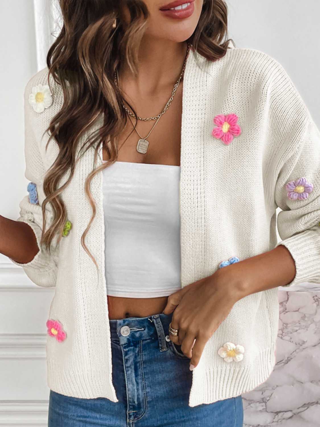 White cardigan featuring vibrant, knitted flower details.