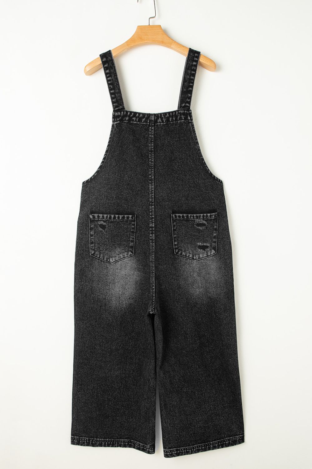 Back view of black washed distressed overalls with two back pockets.
