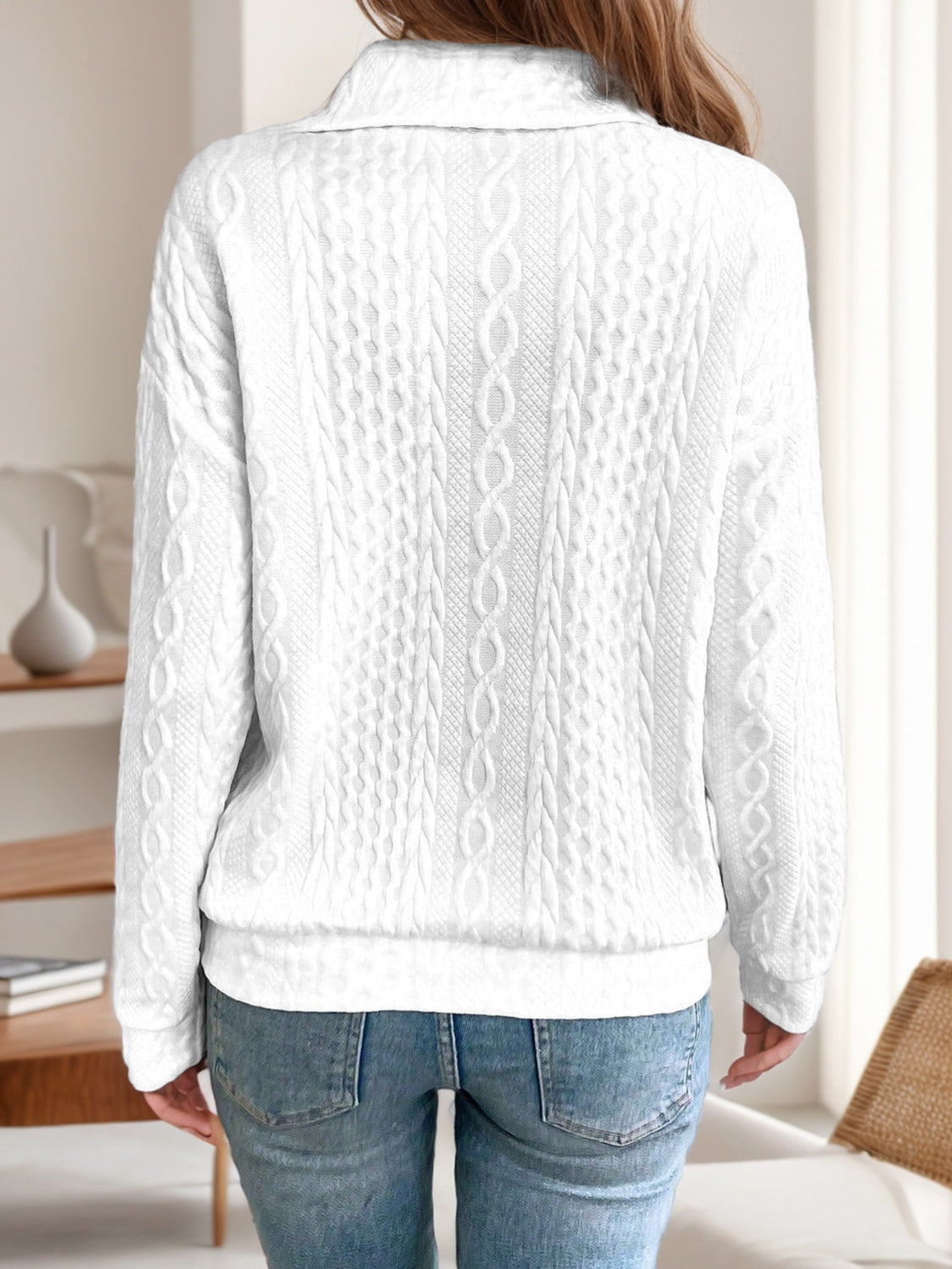 Back view of a white quarter-zip knit sweater, showing its relaxed fit and cable knit detailing.

