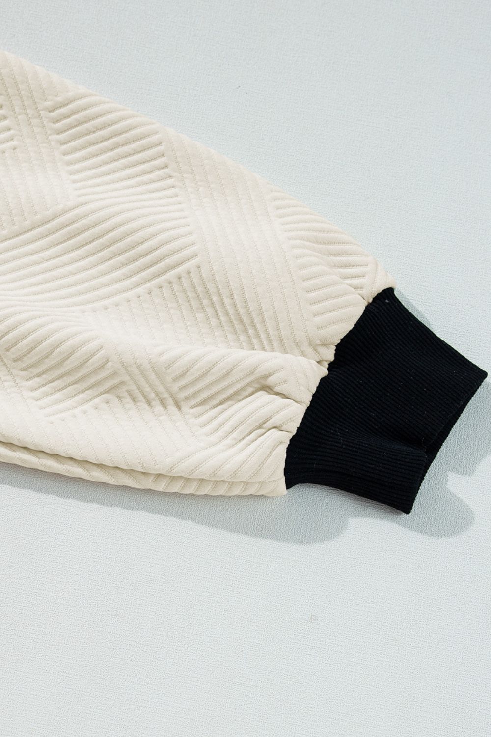 Close-up of the geometric knit pattern on the beige pullover, highlighting the black contrast trim.

