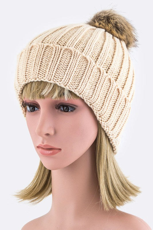 Neutral beige ribbed knit beanie topped with a fluffy faux fur pom.
