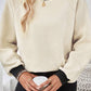 A beige textured sweater with black contrast trim, shown in a relaxed fit for versatile styling.