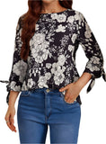 Woman wearing a black and white floral blouse with tied sleeves and relaxed fit.
