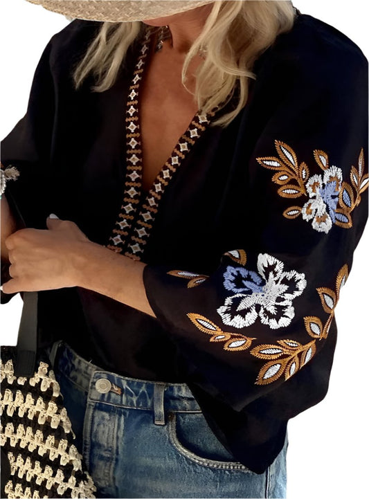 Woman wearing a black boho top with floral embroidery along the sleeves and neckline