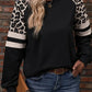 Woman wearing a black sweatshirt with leopard print and white striped sleeve details.
