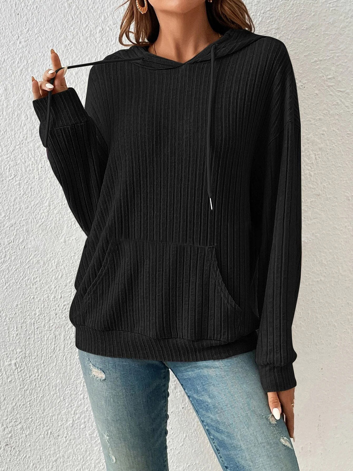 Woman wearing black ribbed drawstring hoodie with front pocket.
