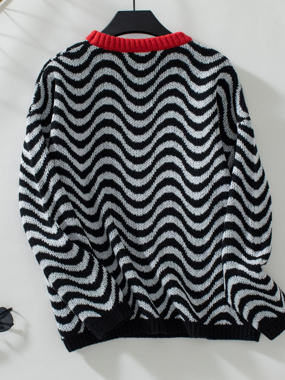 A stylish black striped knit sweater with wavy pattern, paired with casual bottoms.

