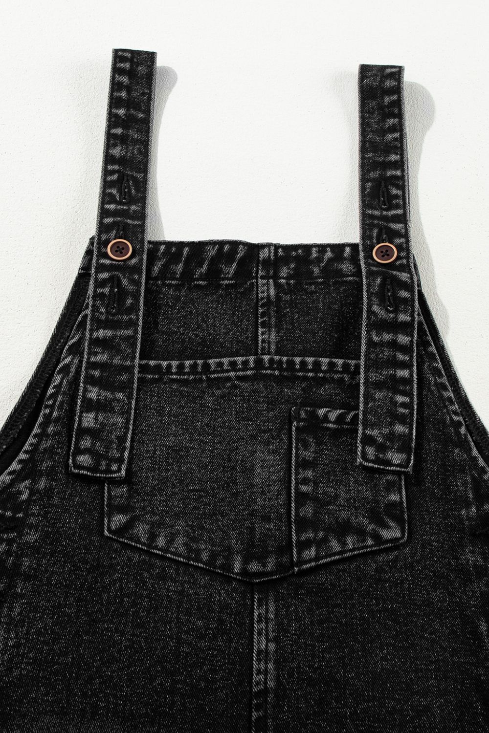 Close-up of distressed detailing and pocket design on denim overalls.
