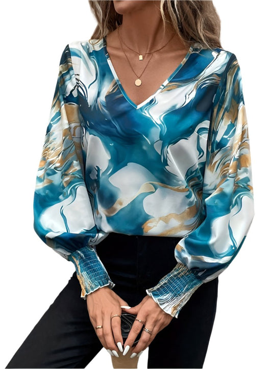 Woman wearing a satin blue marble blouse with V-neck and smocked cuffs.
