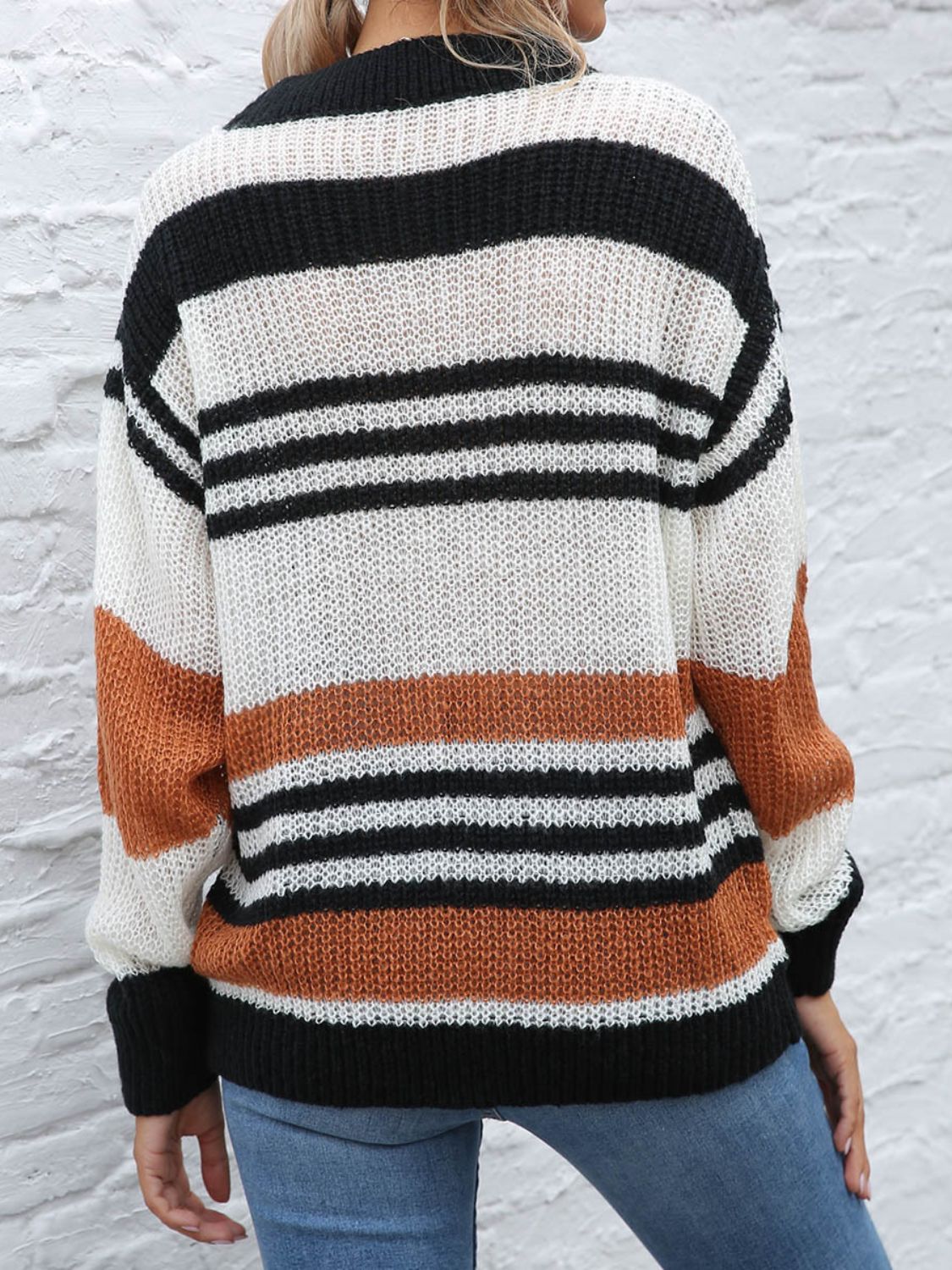 Bold black, white, and orange striped sweater styled with ripped jeans