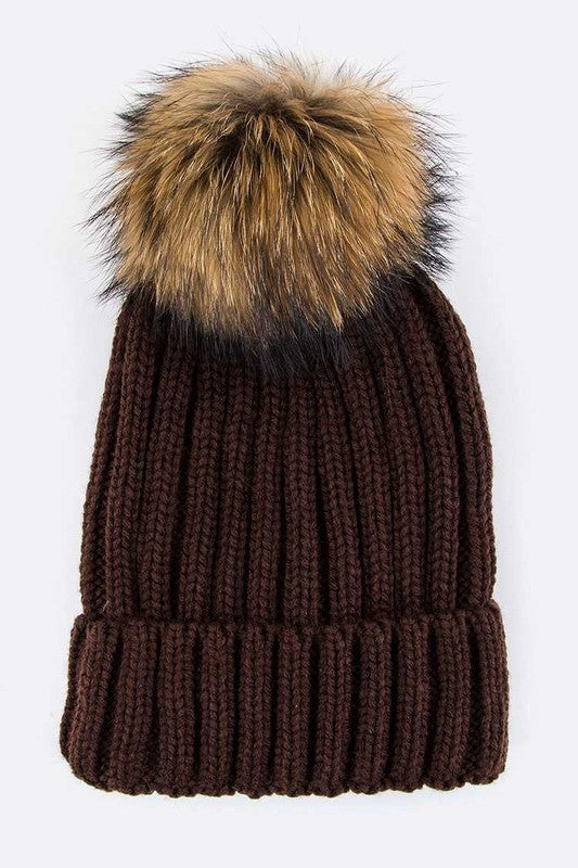 Brown ribbed knit beanie featuring a cozy faux fur pom for warmth.
