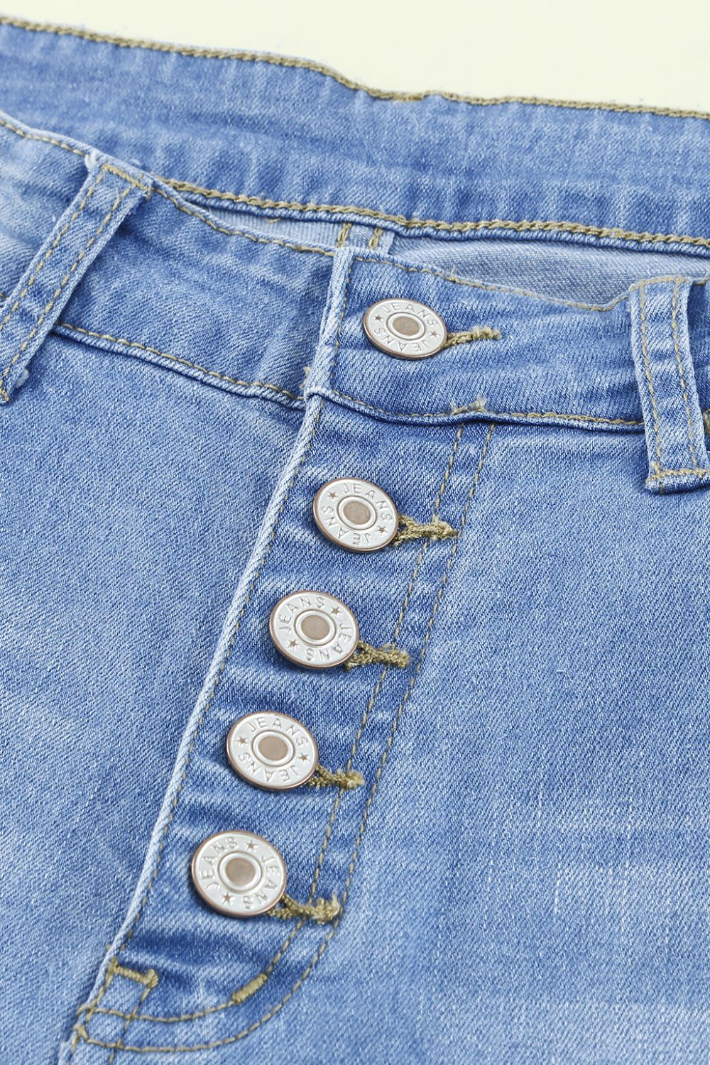 Front view of button-fly distressed raw hem flare jeans in light blue denim with knee distressing and a high waist.