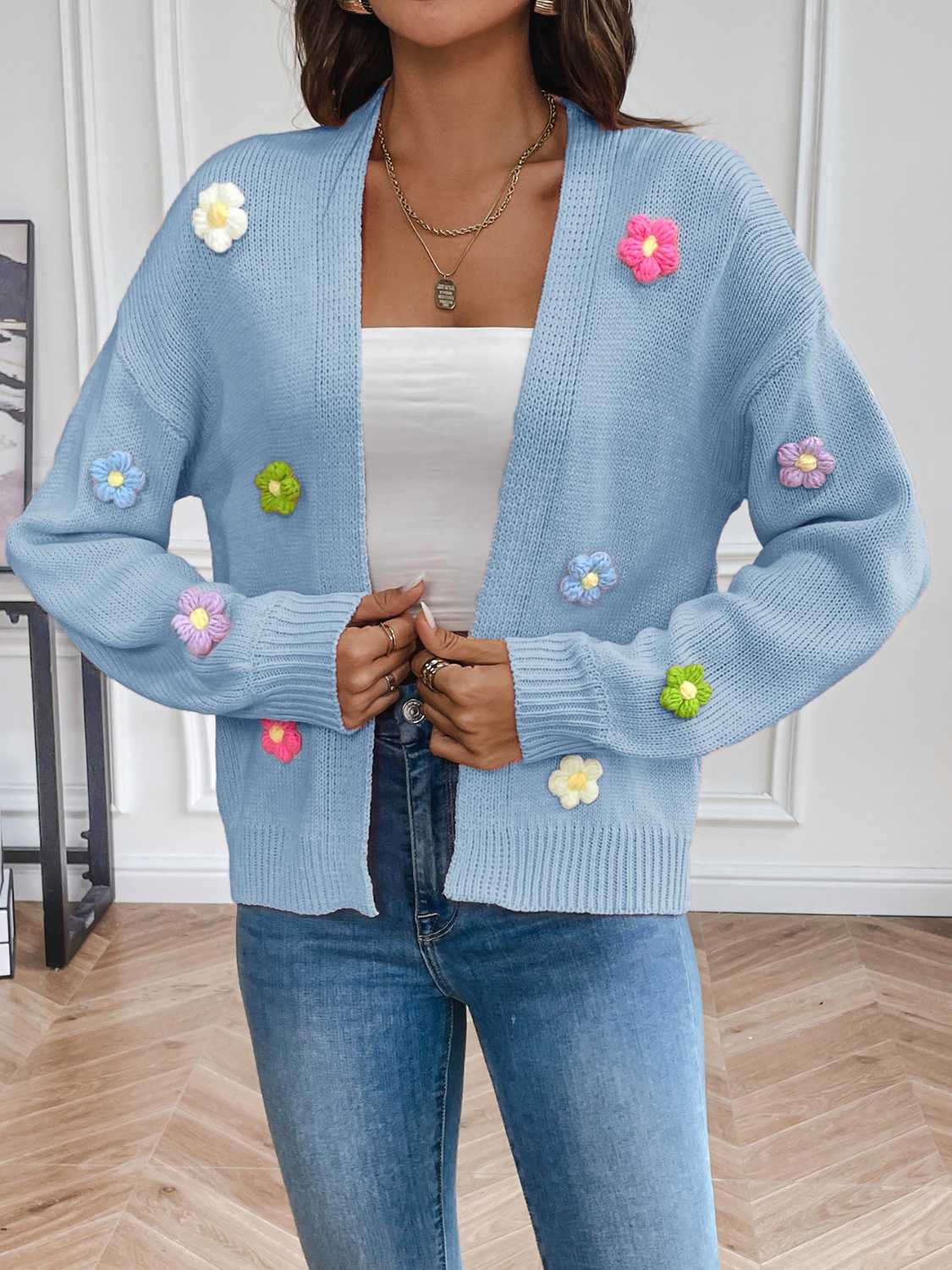 Blue cardigan adorned with pink, yellow, green, and purple knitted flowers.