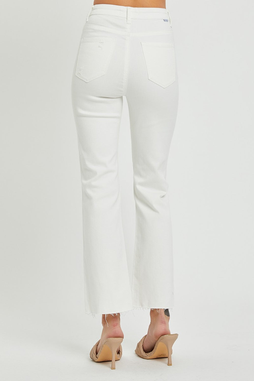 High-rise white jeans featuring knee rips and multiple button closure.