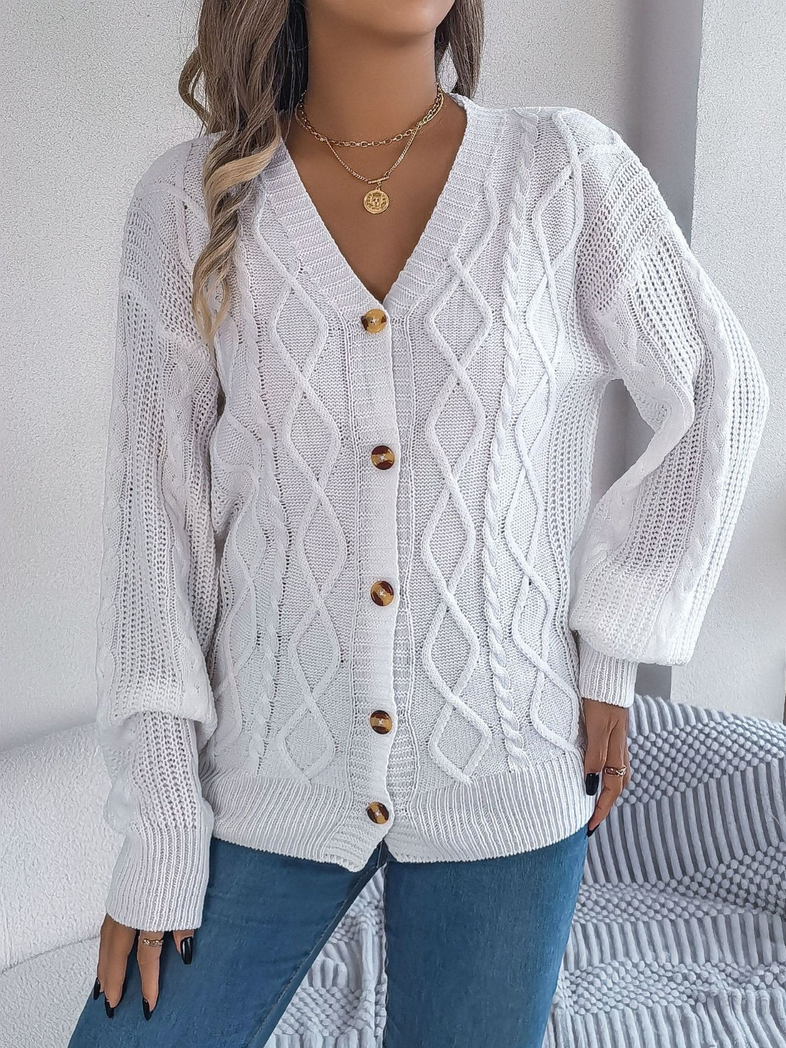 Classic white cable knit cardigan sweater with a cozy design and buttons.
