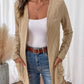 Woman wearing a beige cable knit cardigan with a textured design, styled with a brown belt and denim jeans.