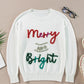 Flat-lay of a white sweater with the "Merry & Bright" tinsel graphic, showcasing its festive style.