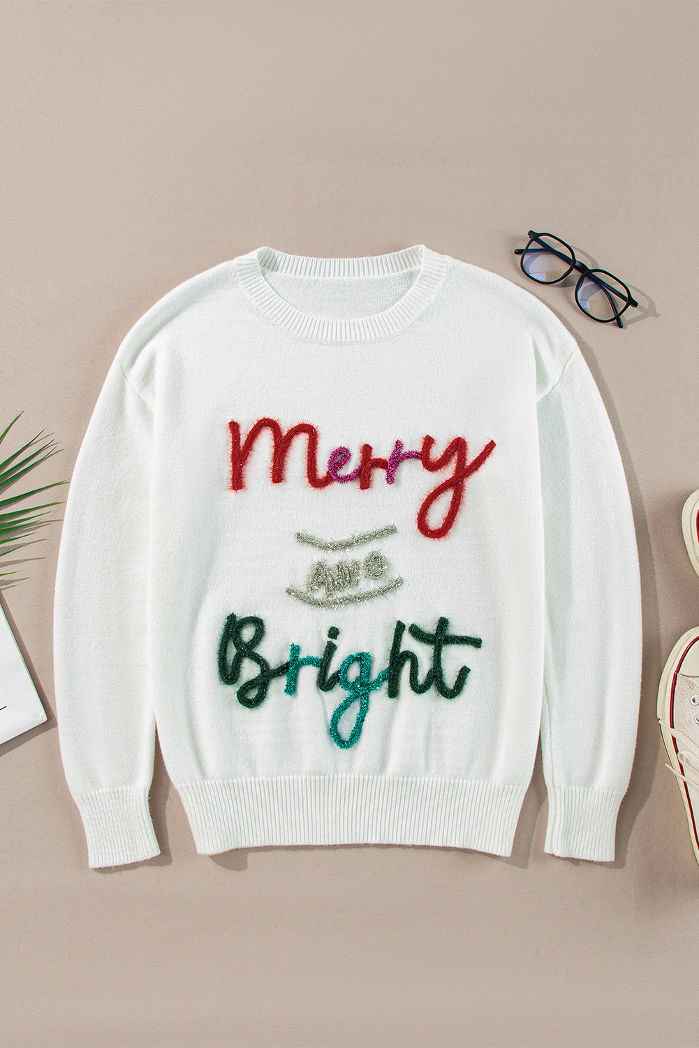 Flat-lay of a white sweater with the "Merry & Bright" tinsel graphic, showcasing its festive style.