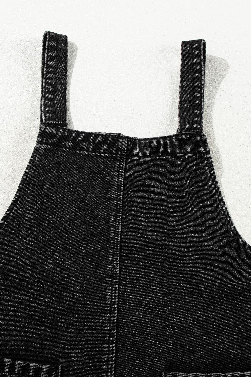 Back view of black washed distressed overalls with two back pockets.
