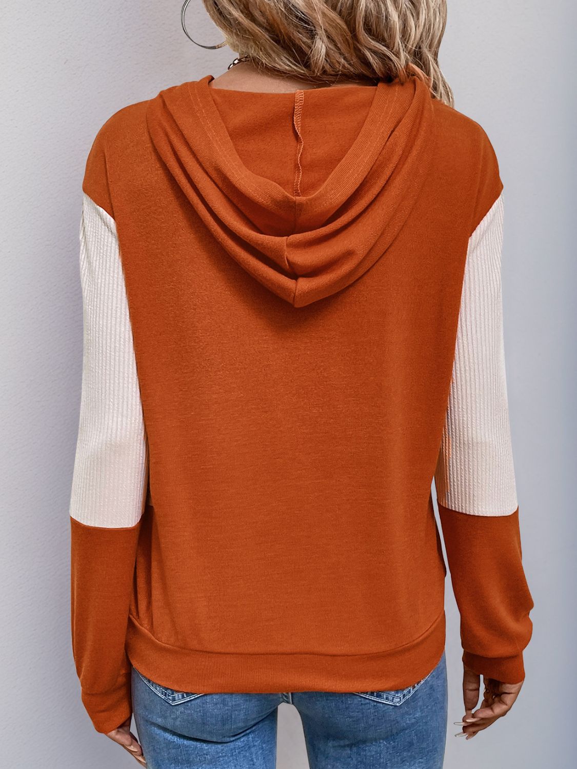 Trendy orange and cream color block hoodie for women, styled with jeans.
