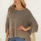 Close-up of a soft knit poncho with fringe detailing along the hemline in a neutral taupe color.