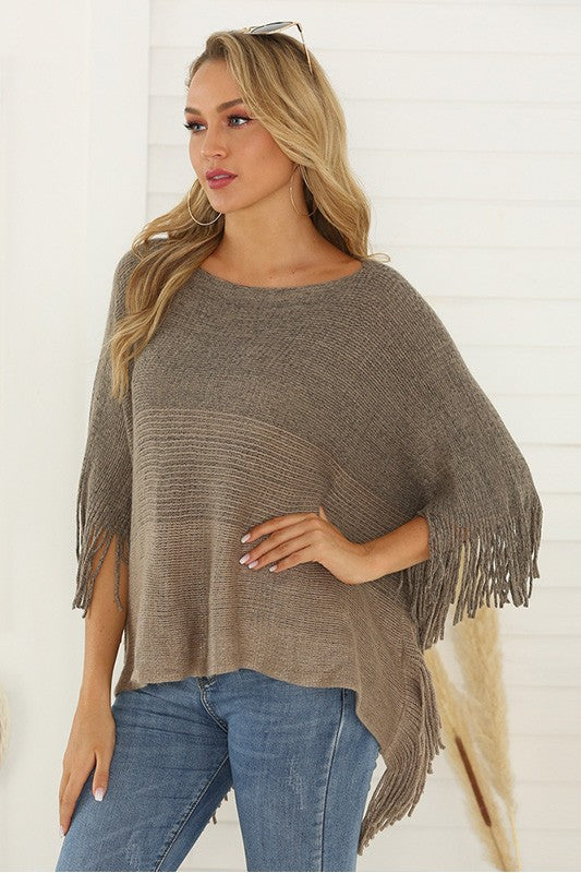 Close-up of a soft knit poncho with fringe detailing along the hemline in a neutral taupe color.