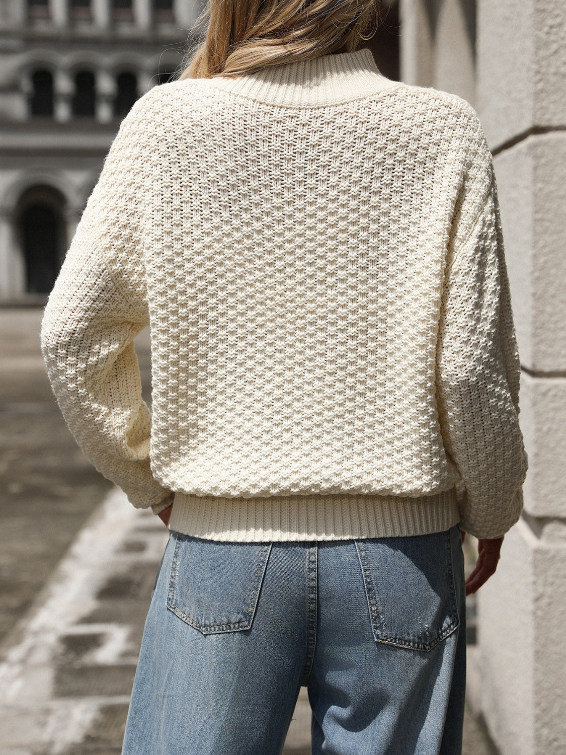 Back view of relaxed fit cream textured knit sweater on woman outdoors
