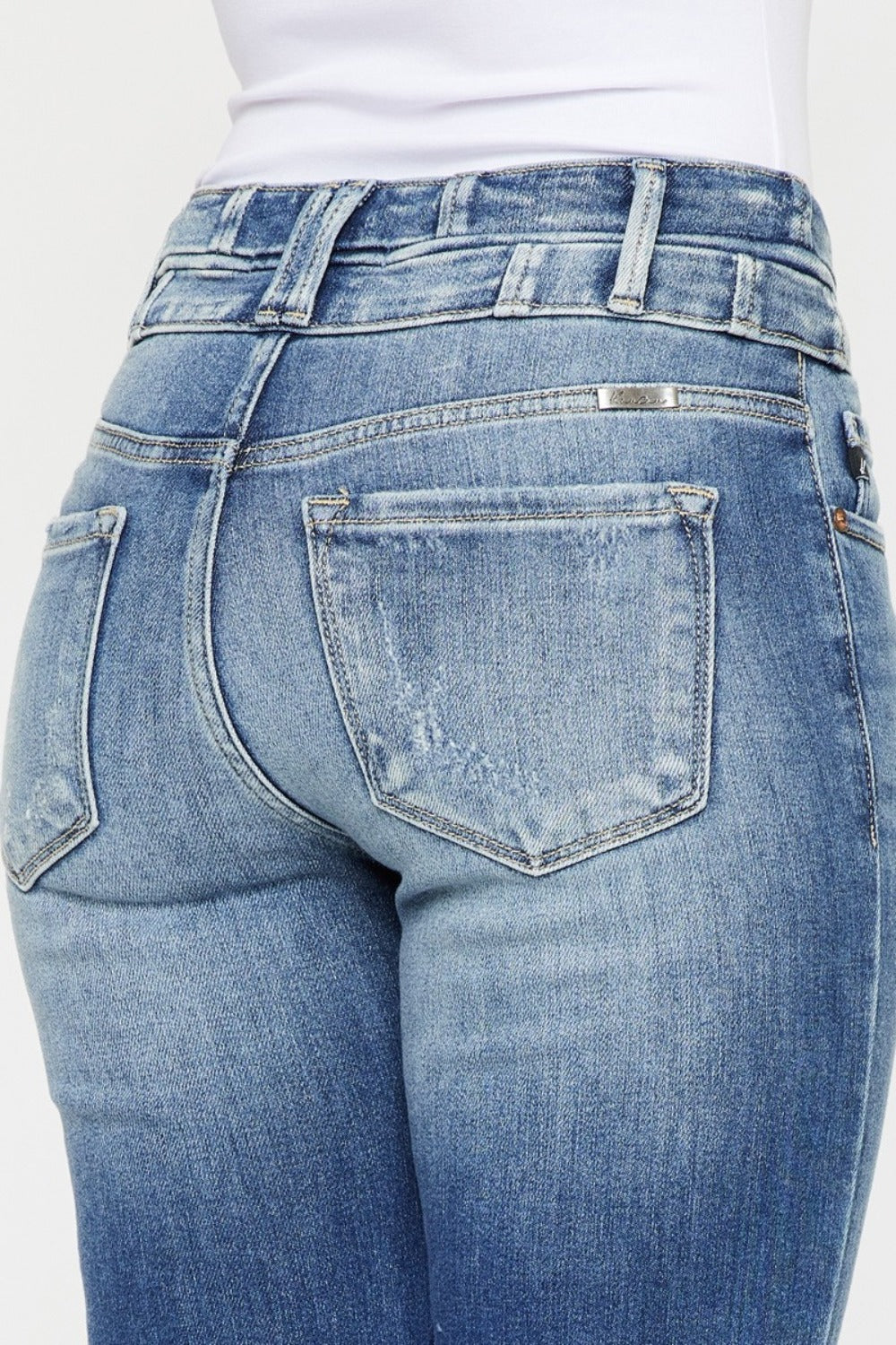 Back view of wide waistband flare jeans with subtle distressing and raw hem.
