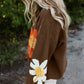 Close-up of brown sweater featuring vibrant flower designs and a V-neck.
