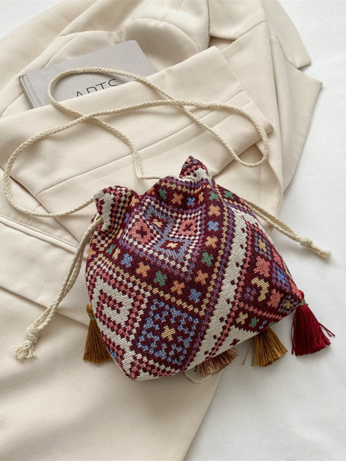 Wine-colored pouch bag with vibrant geometric designs and tassel accents.