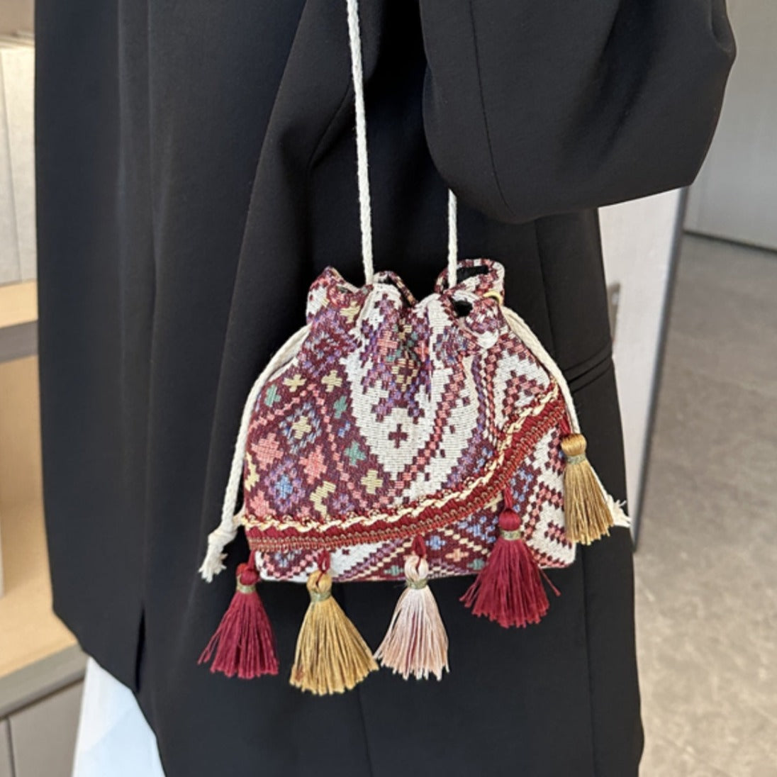 Wine drawstring pouch bag with colorful geometric patterns and playful tassel accents.
