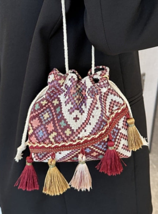 Wine drawstring pouch bag with colorful geometric patterns and playful tassel accents.