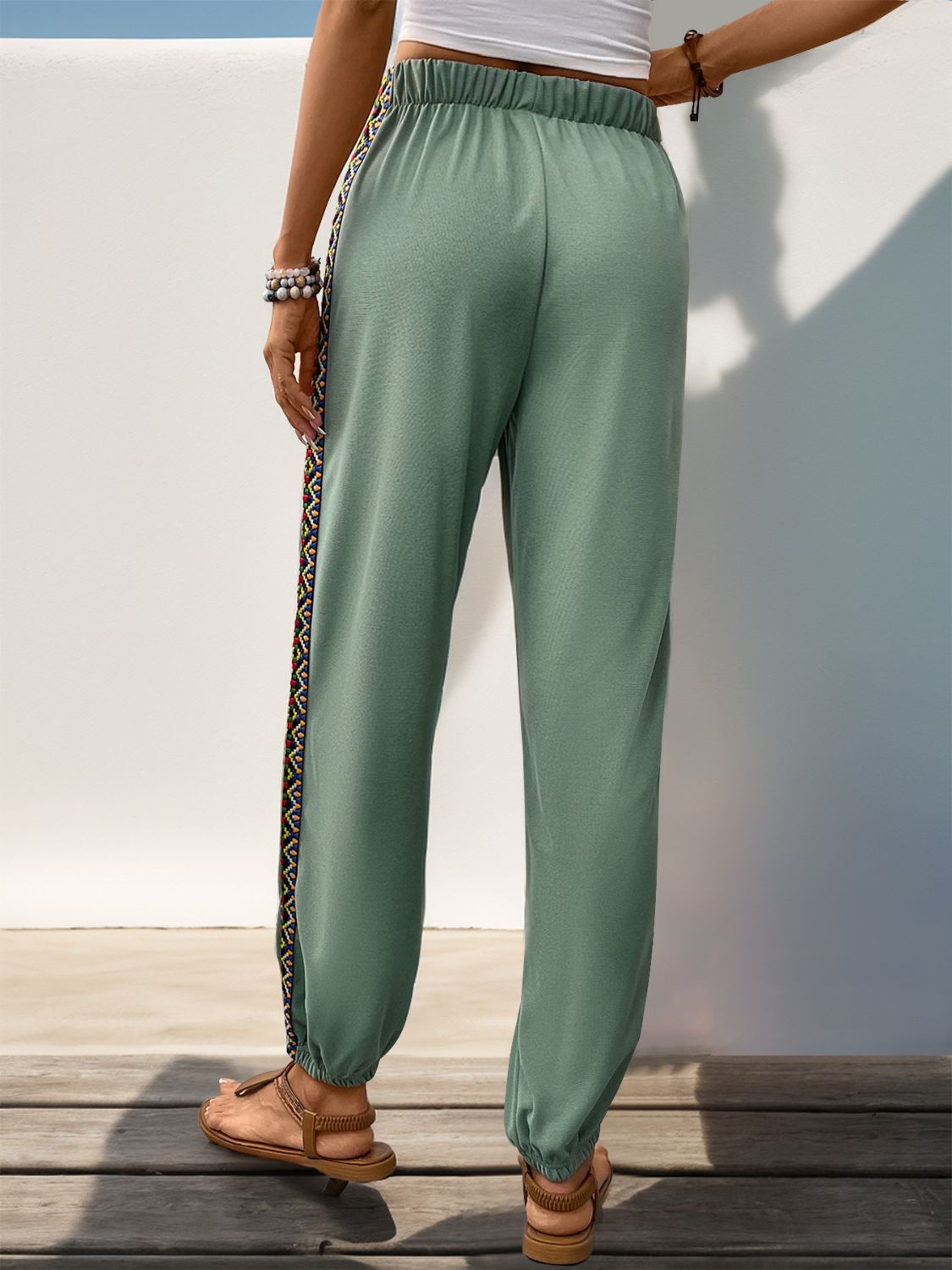 Sage green joggers featuring a vibrant embroidered stripe down the leg.