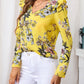 Yellow floral ruffle blouse featuring a vibrant floral print and long sleeves, styled with white pants.
